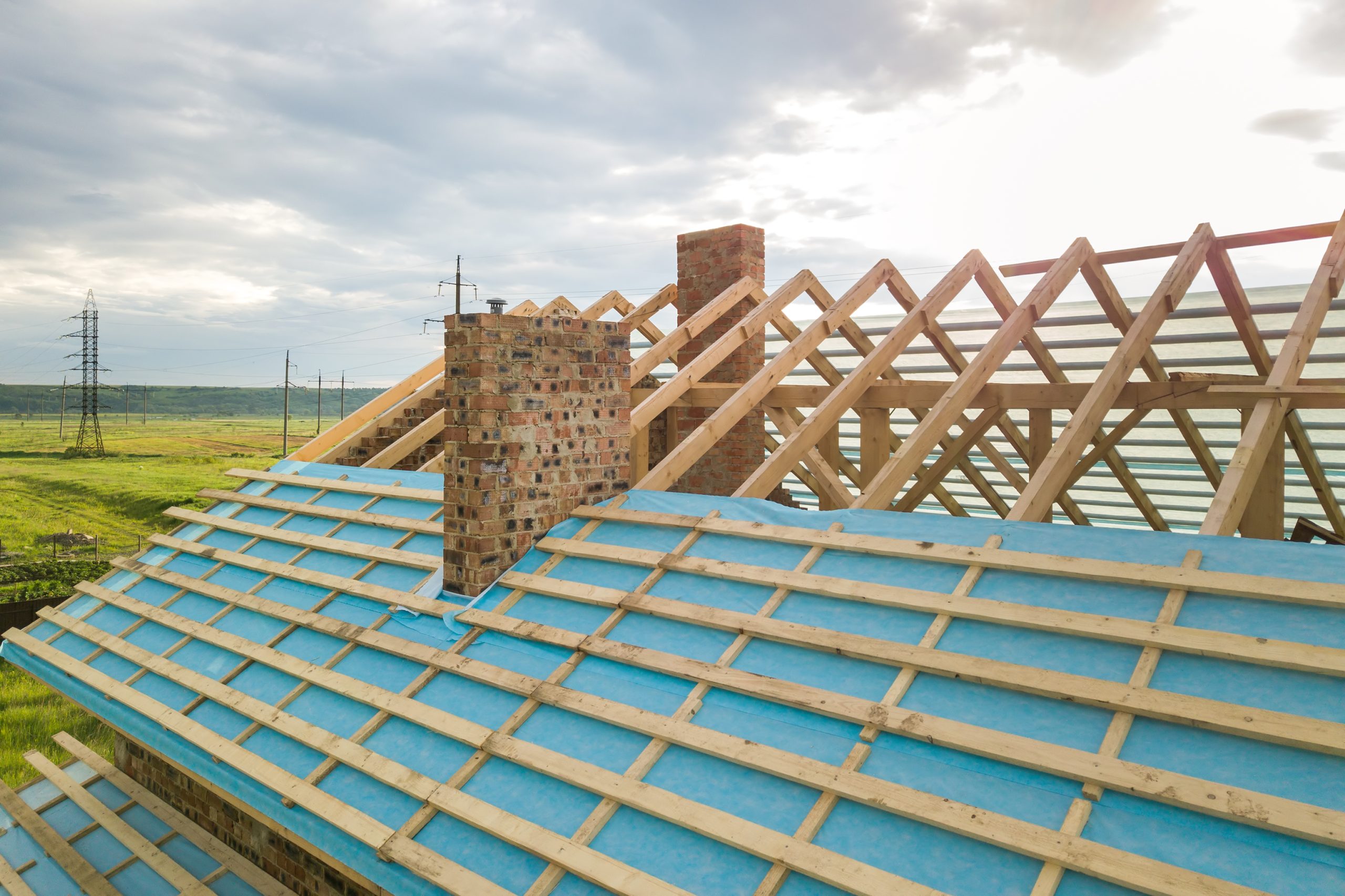 Aerial view of a brick house with wooden roof frame under construction.